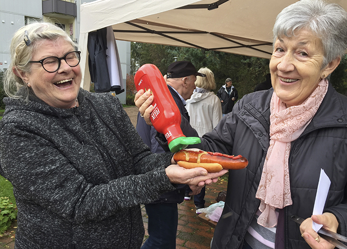 Två glada damer på gårdsfest, där den ena hälle på ketchup på den andras varmkorv