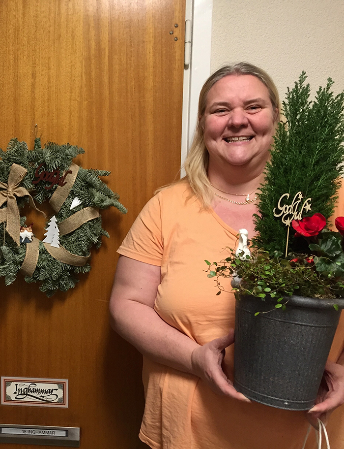 Glad kvinna med blomsteruppsättning i famnen, framför en port med en blomkrans